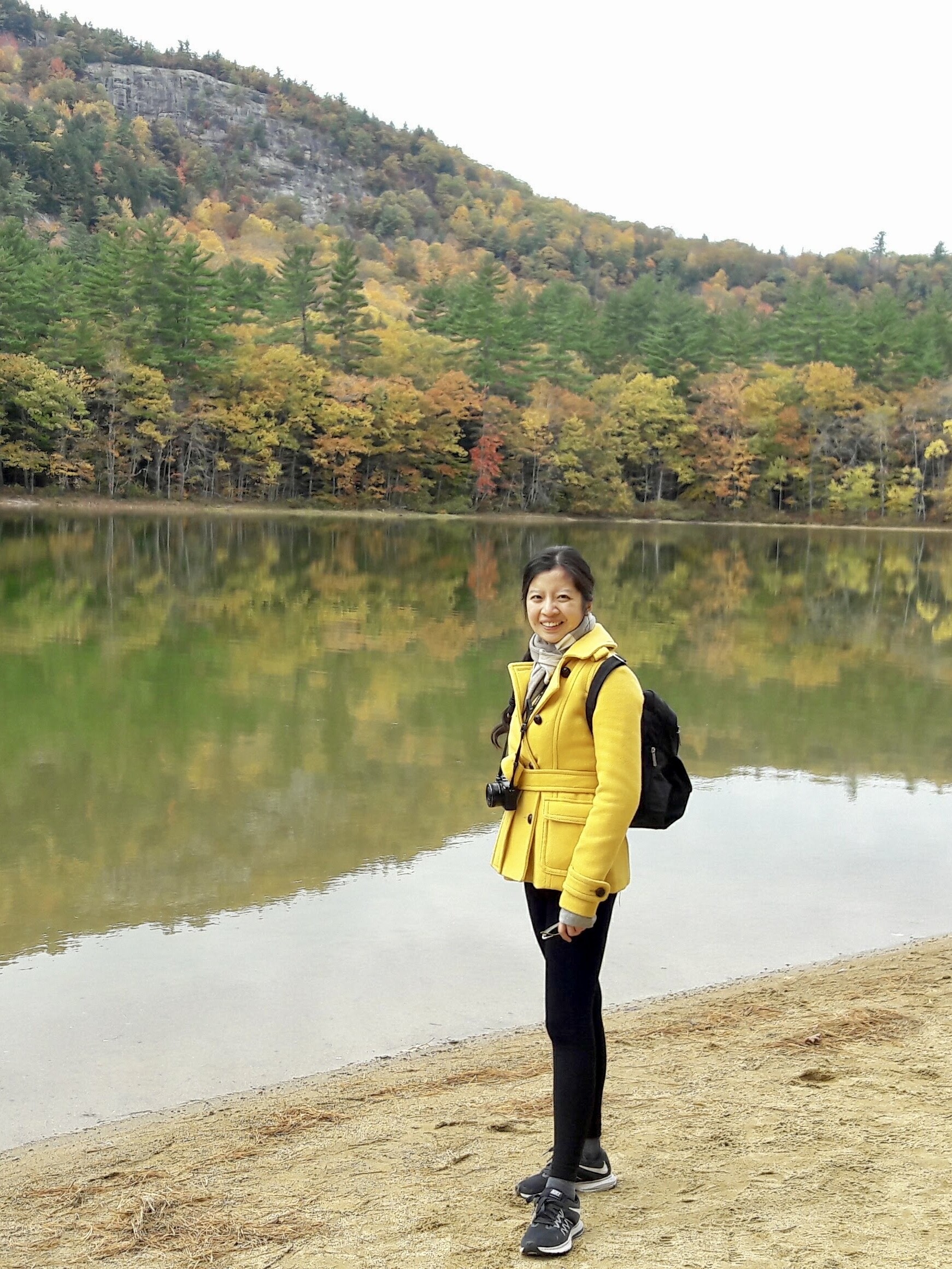 Celestine Hong poses beside a scenic lake with trees in the background.